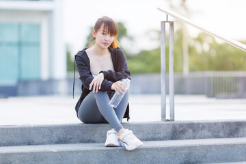 Portrait of beautiful asian Young woman in Black robe sportswear and drinks water working out outside. training on public equipment in outdoor at park. concept Exercise Healthy lifestyle.