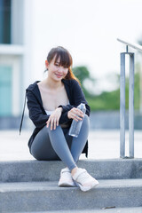 Portrait of beautiful asian Young woman in Black robe sportswear and drinks water working out outside. training on public equipment in outdoor at park. concept Exercise Healthy lifestyle.