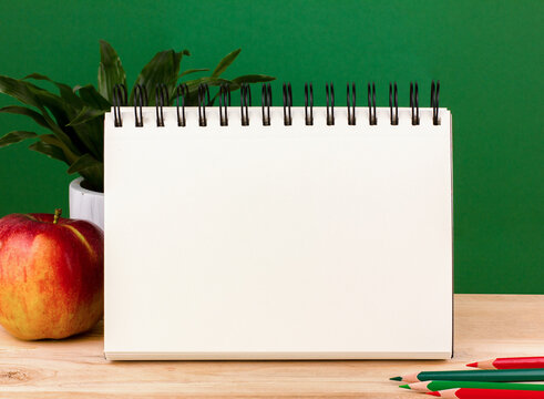 Back to school concept, open notebook,red apple on wooden surface on the backdrop of a clean green chalk board, copy space