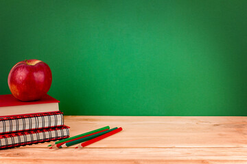 Notebooks, pencils, apple on wooden desk. Education and learning concept on green background