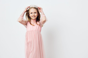 Cheerful young girl in a pink dress and crown, smiling against a neutral background, perfect for...