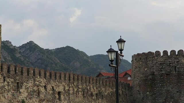 Stone walls of Rabati Castle with lamppost in Akhaltsikhe, Georgia, with mountains and cloudy sky