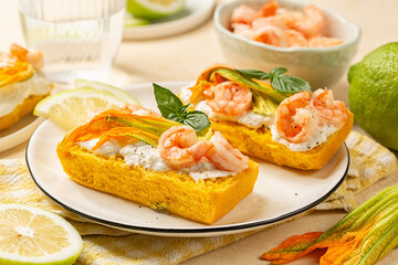 Bruschetta or open sandwich with pumpkin bread, shrimps, prawns and burrata cheese with Zucchini Flowers or Italian Squash Blossom on a white plate.