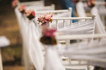Upon a serene summer's day, white chiavari chairs await a joyous ceremony in the outdoor wedding, adorned with delicate pink blossoms and flowing white tulle