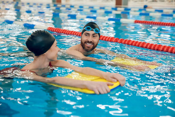 Young cute couple in swimming with boards in the pool