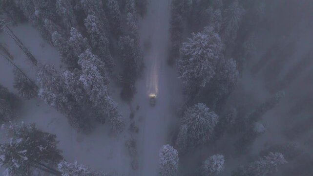 Aerial view of headlights cutting through snow mist on Gulmarg road.