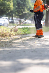 Gardener trimming grass in urban park during daytime with motorized tool to maintain greenery and...