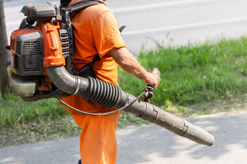 Lawn maintenance worker using leaf blower on a sunny day in a suburban area