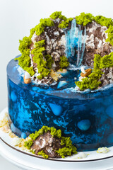 Beautiful birthday cake in the shape of an island decorated with chocolate edible mountains, greenery with waterfall. Tropical island cake surrounded with blue jelly ocean water