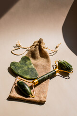 Close up of green quartz gua sha and facial massager on minimalist surface under straight sunlight with hard shadows. Image for cosmetic promotions anti-aging treatments.
