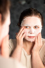 Evening skincare routine. Female applying nourishing face mask. Late night face care. Reflection in bathroom mirror. Dermatology concept.