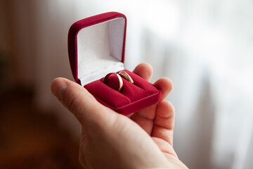 Hand holding red jewelry box with wedding rings