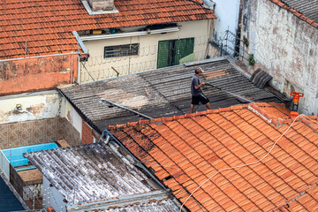 Marilia, SP, Brazil. April,10,2025. Man works on rooftops in a Brazilian city without safety gear,...