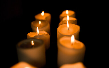 Velas blancas encendidas en fila sobre fondo oscuro, creando una atmósfera cálida y espiritual