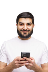 Young man with a dark beard and a white T-shirt smiles while holding and interacting with his smart...