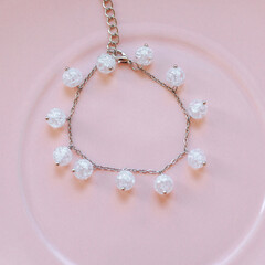 Delicate silver chain bracelet with round crackle glass beads arranged on a pink ceramic plate, top...