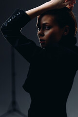 dramatic woman posing in black coat with moody lighting and dark background, expressing mystery and...
