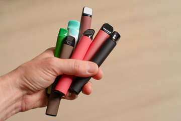 Various disposable electronic cigarettes in a female hand on a light background