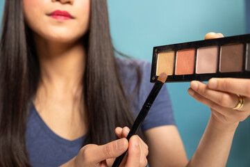 Closeup of female content creator holding a brush and eyeshadow palette, showing the different...