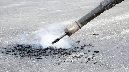 Asphalt repair with a specialized tool emitting steam. Road maintenance in progress with hot materials and equipment on the gray asphalt surface. Close-up on damage fix.