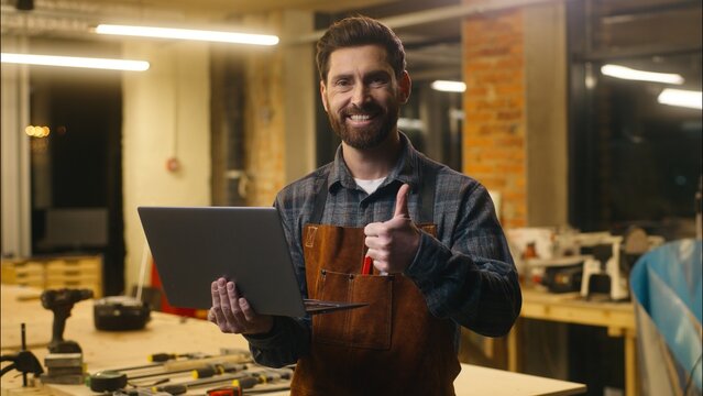 Cheerful Caucasian man carpenter typing laptop showing thumb up sign in workshop wood master male worker artist using Internet delivery app online glad architect guy recommend craftsman satisfaction