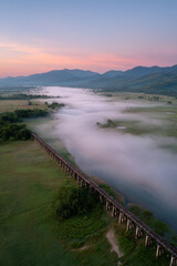 Obraz premium aerial view of misty mountains at dawn with abandoned wooden bridge in foreground