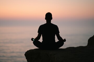 Silhouette of person meditating on cliff during tranquil ocean sunset reflecting peace and