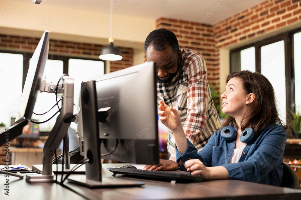 Poster black male manager standing by desk, discussing product designs with caucasian employee working on c