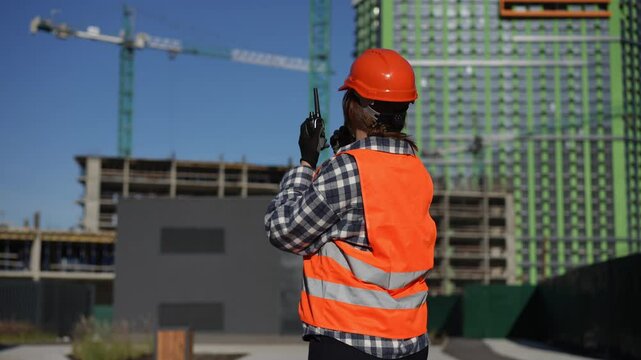 A safe ty clad construction worker is communicating effectively at a busy building site with cranes in the background