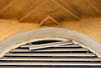 Damaged metal shutter in arched window of old building. Urban decay and architectural texture in city street. Grunge detail of neglected facade
