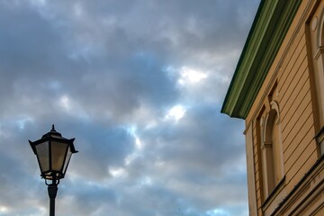 Classic street lamp and building facade against dramatic cloudy sky. Urban atmosphere, vintage...