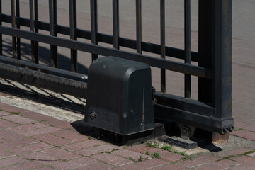 Automated sliding iron gate and motor on a brick driveway
