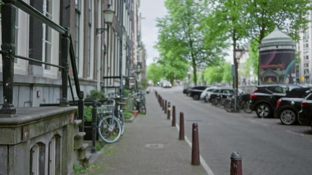 Blurry view of bikes parked on a city street in amsterdam with old buildings and green trees creating a peaceful urban scene.