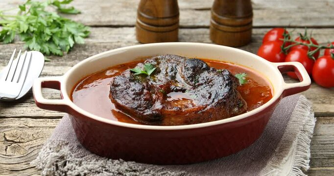 Traditional ossobuco dish with beef steak served on wooden table, closeup. Camera moving