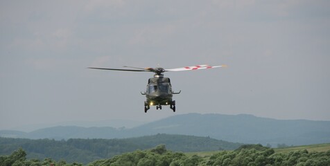 military transport helicopter with its landing gear down hovered over the ground as it approaches...