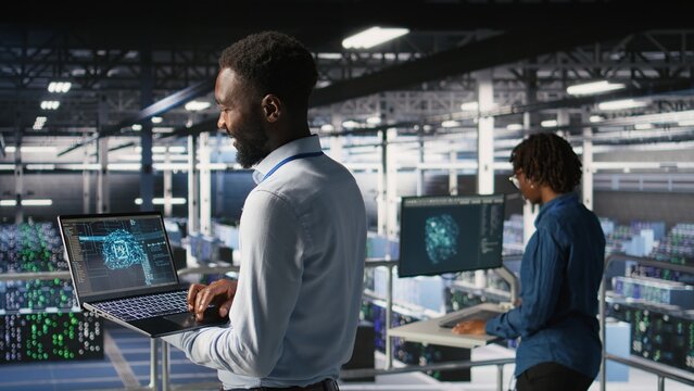 Programmer and colleague in data center reviewing AI LLM visualizations on laptop. IT teamworking coworkers analyze neural network performance outputs to ensure stable infrastructure operations - Powered by Adobe