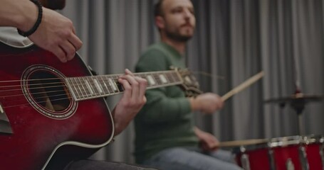 Two musicians practice playing the guitar and drums in a studio. They are preparing for their upcoming concert and working on timing.