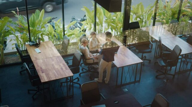 Three business managers in coworking space discussing strategy and projects during productive meeting in modern office with windows and view of vibrant greenery. Coworking place for your success