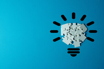 A lightbulb shape filled with jumbled jigsaw puzzle pieces on light blue background with...