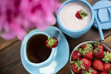 A glass of strawberry milkshake. Pink peonies and red strawberries