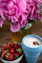 A glass of strawberry milkshake. Pink peonies and red strawberries