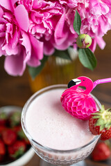 A glass of strawberry milkshake. Pink peonies and red strawberries