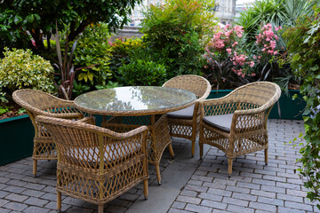 A cozy outdoor seating area with four rattan chairs and a round table surrounded by lush green plants and vibrant flowers
