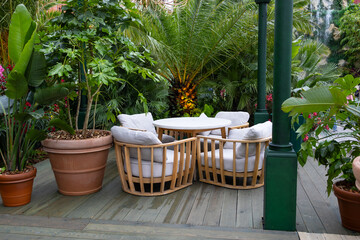 A cozy outdoor seating area with four rattan chairs and a round table surrounded by lush green plants and vibrant flowers