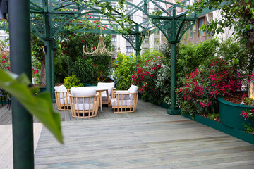 A cozy outdoor seating area with four rattan chairs and a round table surrounded by lush green plants and vibrant flowers
