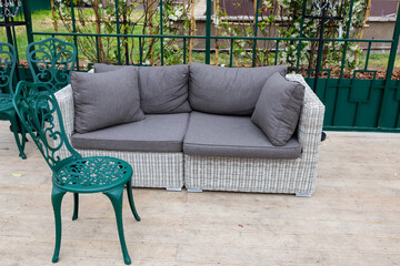A modern grey sofa with cushions is installed in a glass greenhouse outside. Lush green plants and vibrant flowers surround the living area, creating a serene atmosphere.