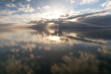 Obraz premium Drone Aerial View, Golden sunbeams pierce through clouds, reflecting on the tranquil waters of IJsselmeer Lake during a peaceful sunset in the Netherlands.