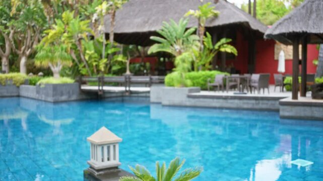 Blurred tropical resort scene with luxurious pool and lush greenery enhancing the outdoor hotel ambiance in a defocused composition.
