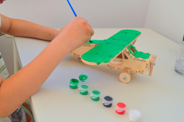 Painting wooden airplane model with green paint in creative art workshop