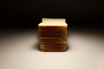Vertical stack of white sandwich bread slices on white surface with moody dark background and soft studio lighting. Minimalist food concept. High resolution close-up photo